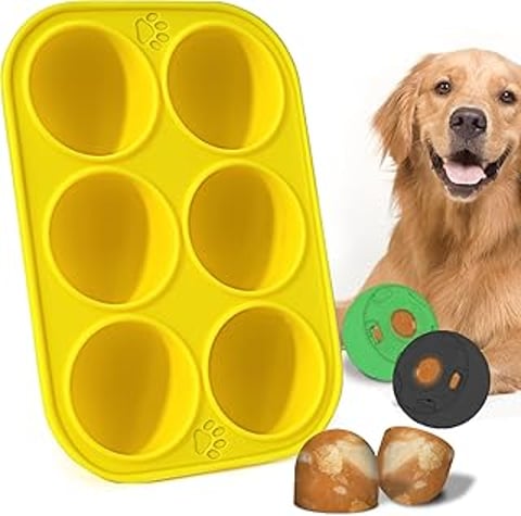 A dog is sitting next to a yellow container with a green ball inside.