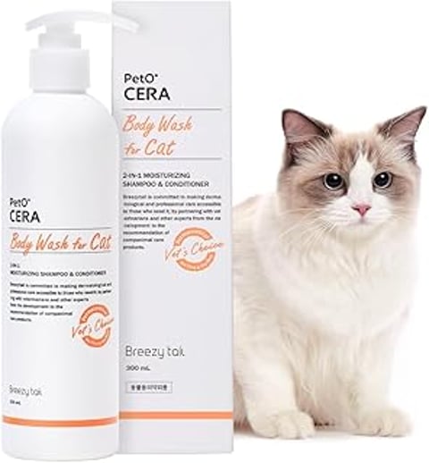 A cat is sitting next to a bottle of PetO'Cera body wash for cats.