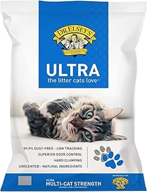 A cat is laying on a white surface with a bag of Dr. Elsey's Ultra litter.