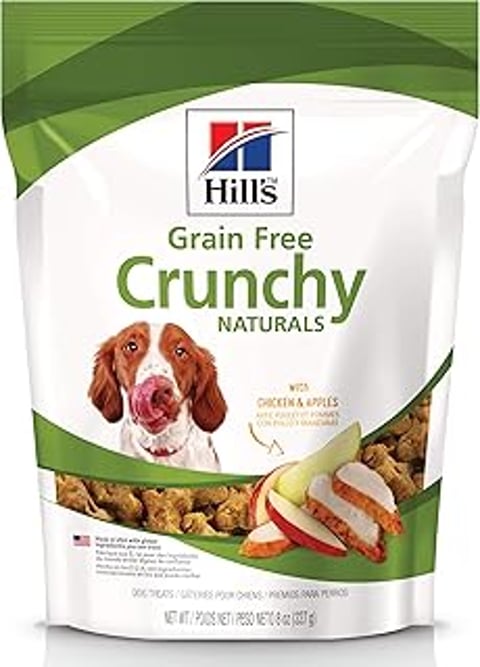 A dog with a pink tongue licking a bag of Hill's Natural Grain Free Crunchy Dog food.