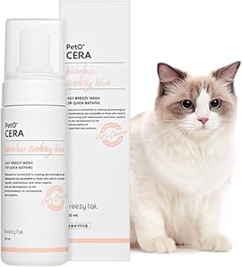 A cat is sitting next to a bottle of PetO'Cera waterless shampoo.