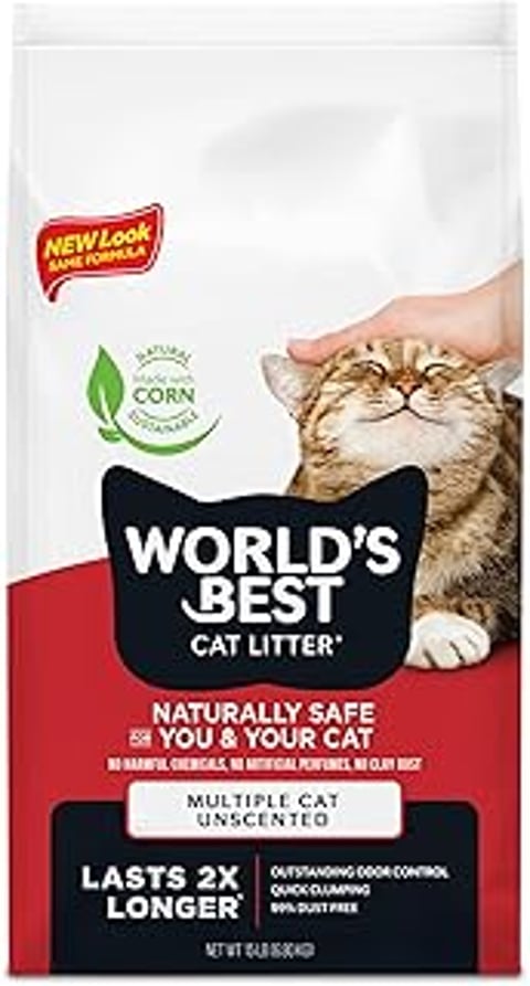A cat is being petted by a person while sitting on a bag of World's Best Cat Litter.